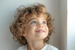 A cheerful Caucasian boy with curly hair gazes upwards, illuminated by soft natural light, showcasing his joyful expression. photo