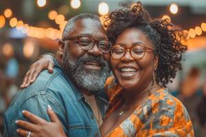 A joyful Black couple smiles together, illuminated by soft, warm lights at a vibrant outdoor gathering. photo