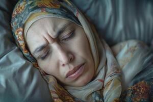 A Middle-Eastern woman with a headscarf resting her head on soft pillows, displaying a contemplative expression. photo