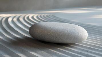 A smooth, gray pebble rests on meticulously raked sand in a tranquil setting. photo