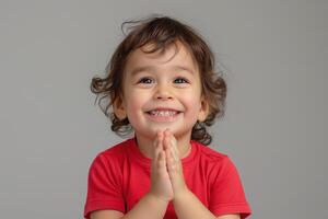 A joyful toddler with curly hair and a bright smile, clasping hands in excitement against a neutral background. photo