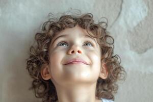 A joyful young child with curly hair gazes upward, radiating innocence and happiness against a soft, textured background. photo