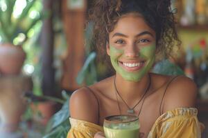 A joyful young woman of mixed ethnicity with a green face mask smiles brightly while holding a cup of green beverage. photo