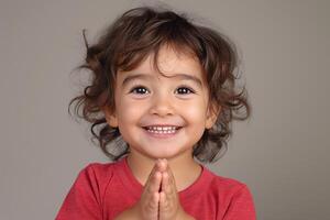A joyful young boy of Hispanic descent with curly hair expresses happiness, clasping his hands together in a playful manner. photo