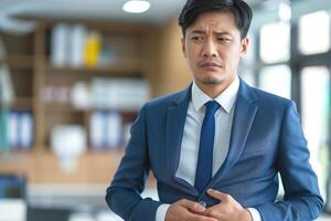 Concerned Asian businessman in a blue suit, expressing discomfort in a modern office setting. photo