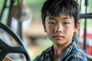 A focused young Asian boy sits behind the wheel of a vehicle, showcasing determination and curiosity. photo