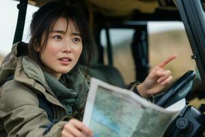 A thoughtful young Asian woman navigates with a map while sitting in a rugged vehicle, embodying the spirit of adventure. photo