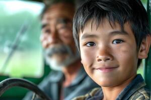 A cheerful Asian boy smiles at the camera while sitting in a vintage vehicle, with an elderly man in the background. photo