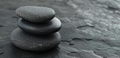 Three stacked black stones on a textured dark surface, symbolizing balance and tranquility. photo