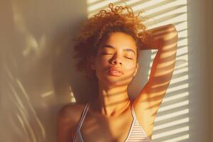 A young mixed-race woman with curly hair relaxes in soft sunlight, casting playful shadows across her face and body. photo