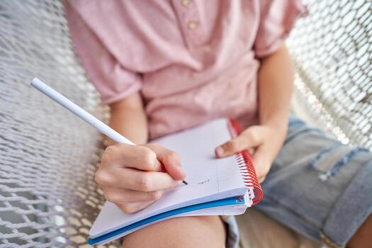 Crop boy lying in hammock and taking notes in notepad photo