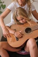 Crop mother and daughter playing guitar together at home photo