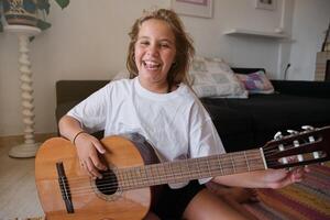 Smiling girl looking at camera while tuning a guitar in a house photo