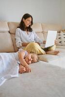 Mother using netbook while sitting on sofa near sleeping baby photo