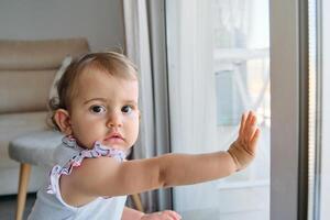 Curious toddler touching window and looking at camera photo