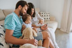 Happy parents with baby using smartphone on sofa photo