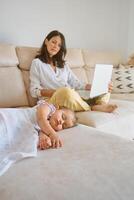 Woman browsing netbook while sitting on sofa near napping baby photo