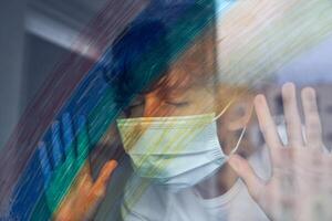 Boy in mask with hands on window at home photo