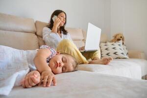 Sleeping daughter resting near mother with laptop and smartphone photo