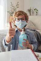 Boy in mask and with sanitizer showing thumb up photo