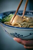 Crop person with boiled egg between chopsticks in ramen photo