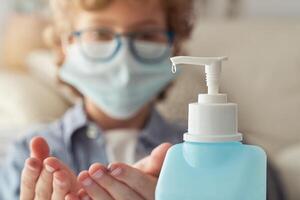 Crop child in mask applying sanitizer on hands photo
