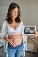 Happy pregnant lady with ultrasound image at home photo