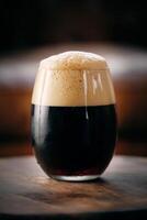 Glass of fresh stout with froth on wooden table photo