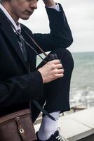 Portrait of a young man against the backdrop of the sea, he is looking into the distance through binoculars. He has long hair, is wearing a suit and tie. Relaxed, peaceful, thoughtful, happy and free on the seashore photo