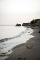Calm, evening beach scene with sandy shore and splashing waves. Rocks are visible at the end of the beach. Calm atmosphere without people. photo