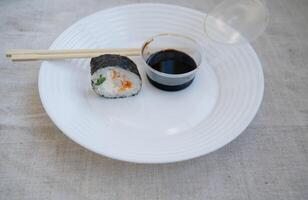 sushi roll with chopsticks and wasabi sauce in a plastic container on a white plate. elements of japanese cuisine, takeaway food. linen tablecloth on the table. photo