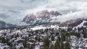 Cortina d'Ampezzo's snow covered rooftops and pine trees with Dolomite peaks in the background, low clouds drifting across the rugged landscape. video