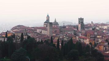 Panoramic view of Bergamo's old town in Italy, showcasing medieval architecture, red tiled rooftops, and landmarks under warm sunset hues. video