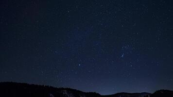 Timelapse of a clear night sky with moving stars and constellations above snow capped peaks, highlighting Earth's rotation in a remote landscape. video