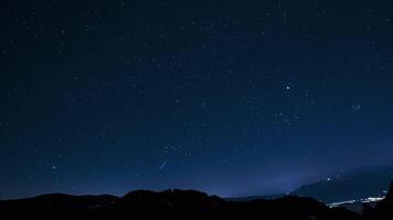 Timelapse showing stars moving across a clear night sky, with mountain silhouettes in the foreground and faint city lights at the base. video
