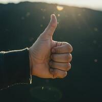 A person giving the thumbs up with the sun in the background photo