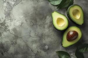Sliced Avocado Halves with Leaves on Gray Textured Background Close Up photo