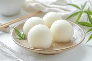 Enjoying Mochi Dumplings on Plate with Chopsticks and Green Leaf photo