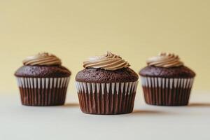 Three Chocolate Cupcakes with Light Brown Frosting on a Yellow Background photo