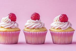 Three Fresh Cupcakes with Raspberry Topping on Pink Background Display photo