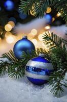 Blue Christmas Ornaments on Snowy Evergreen Branch with Warm Bokeh Lights photo