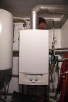 A non-energy-efficient old working gas boiler for home heating, installed in a separate boiler room with a water heater and other outdated heating systems photo