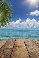 Tropical Beach Scene with Palm Frond, Ocean View and Wooden Deck photo