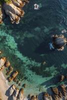 Aerial View of Rocky Coastline with Clear Turquoise Water and Small Beach photo