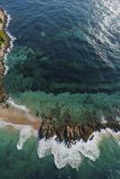 Aerial View of Waves Crashing on Rocky Coastline with Sandy Beach photo