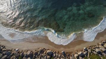 Aerial View of Waves Crashing on Shore with Rocks and Clear Water photo