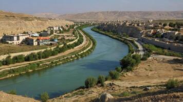 River Flows Through Arid Landscape with Settlements and Distant Mountains photo