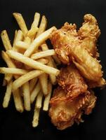 Serving of Crispy Fish and Chips on Black Background for Dinner photo