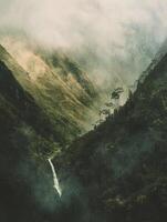 Waterfall in Lush Green Mountain Valley with Mist and Moody Atmosphere photo