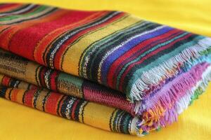 Stack of Colorful Striped Wool Shawls with Fringe on Yellow Surface photo